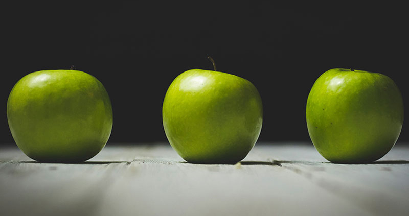 Three green apples on a light wood surface