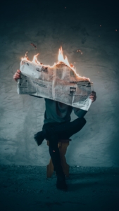 Man sitting on bench holding burning newspaper.