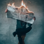 Man sitting on bench holding burning newspaper.