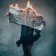 Man sitting on bench holding burning newspaper.