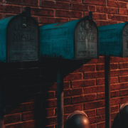 Three green mailboxes against a brick wall in low light