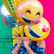 Woman standing in front of colorful wall holding smiley face balloon over her face