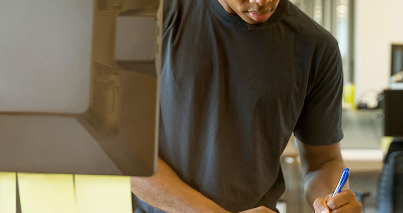 Man jotting down notes next to a computer