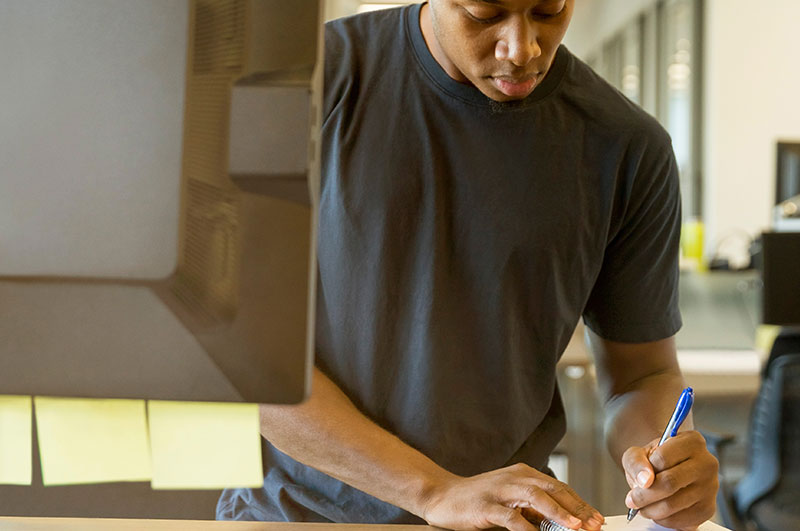 Man jotting down notes next to a computer