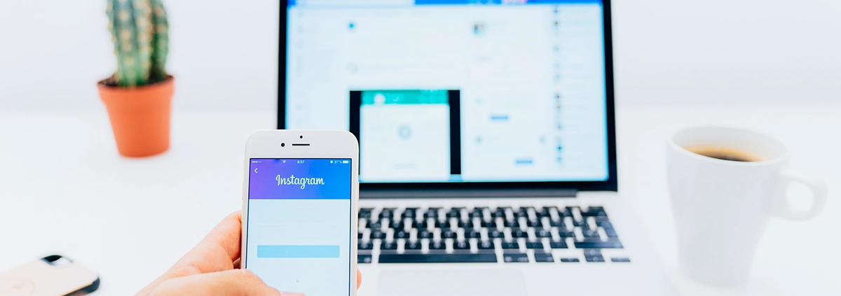 A person logging into Instagram on their phone while sitting in front of a laptop.