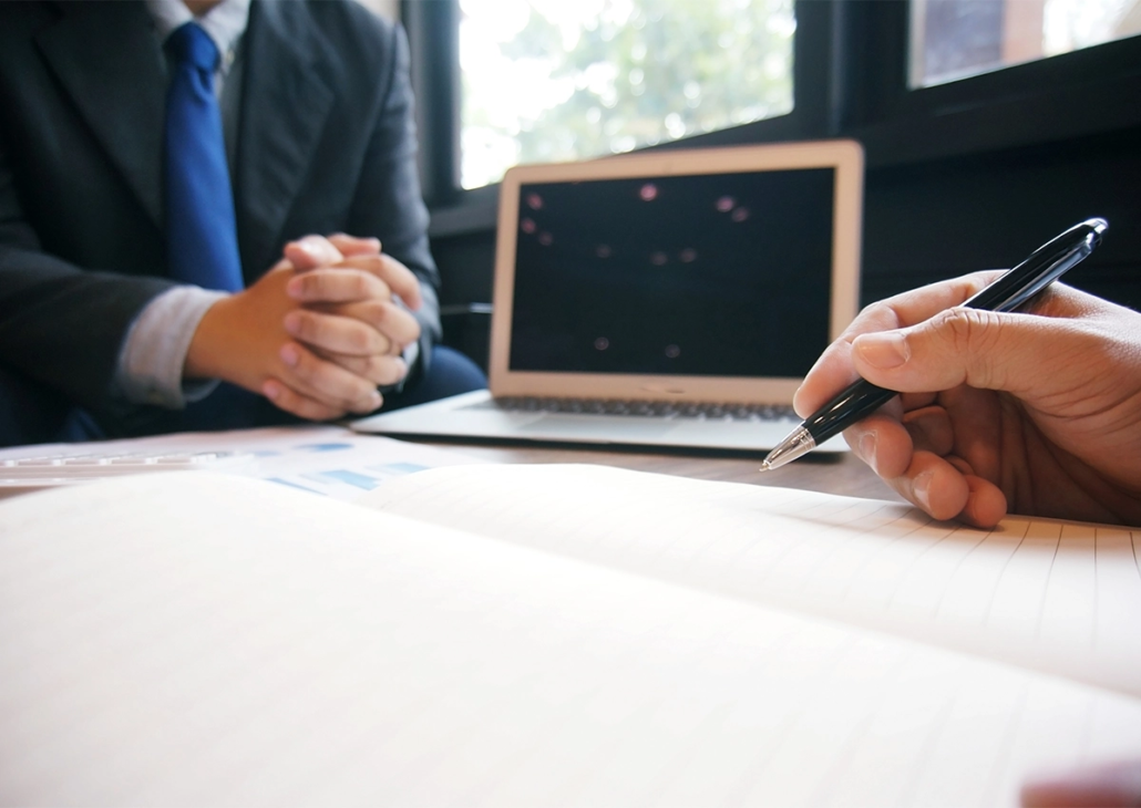 Two people meeting at a table, with a laptop and a pen and paper.